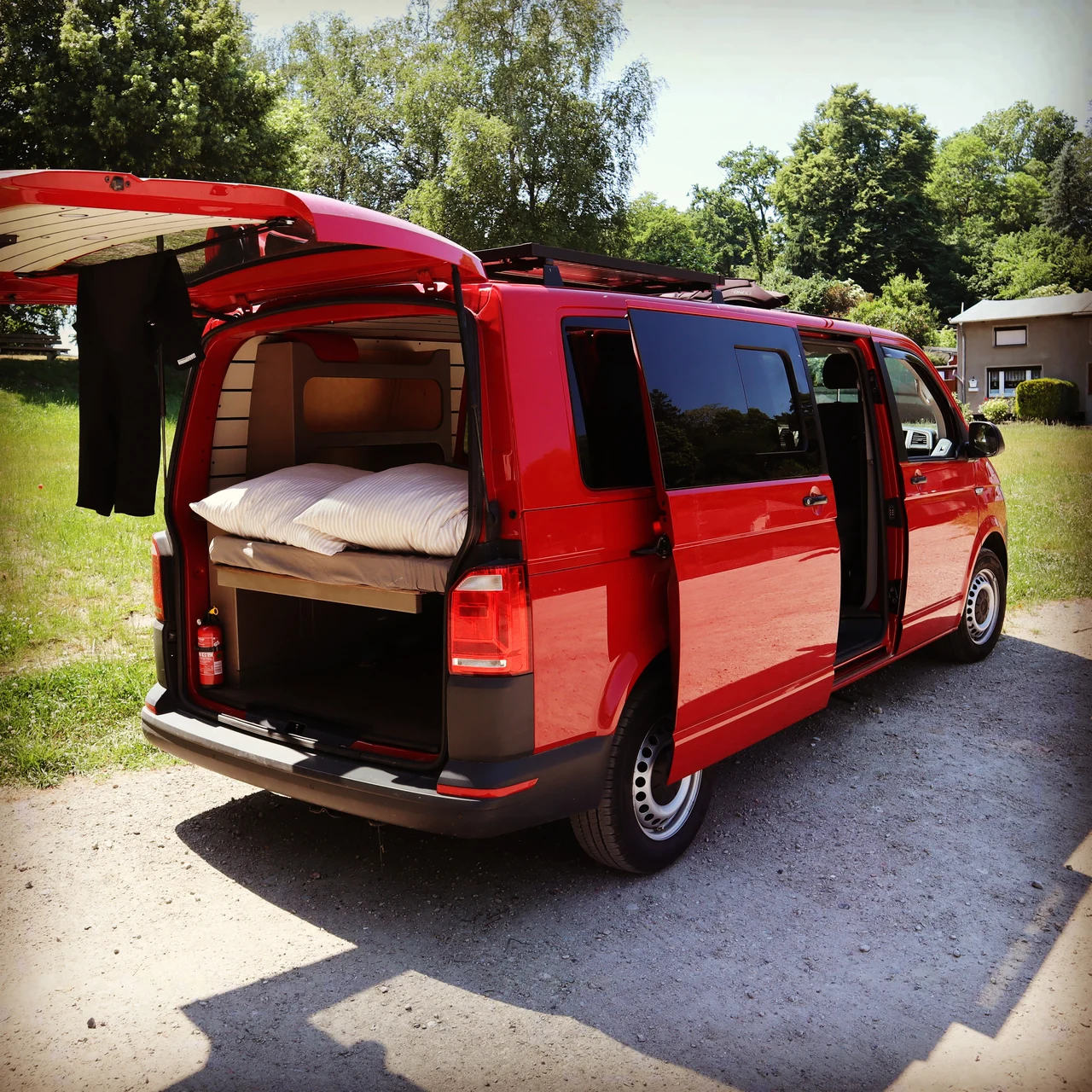 Roter Camper mit offener Heckklappe, gemütlichem Bett und sommerlichem Grün